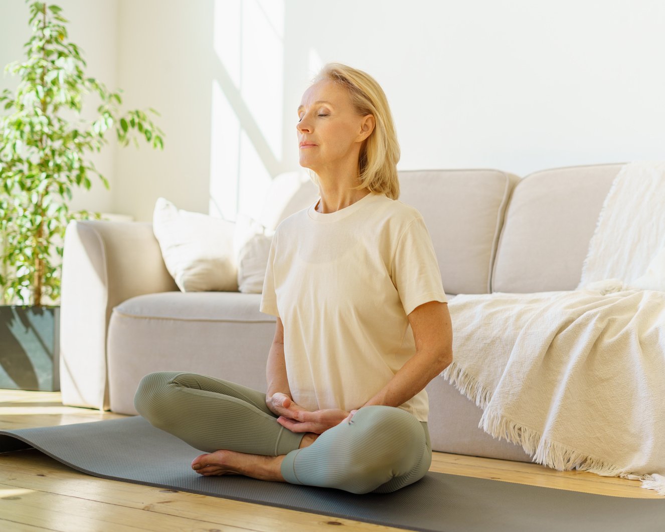 Retired woman meditating and practicing yoga while sitting in lotus pose on floor at home